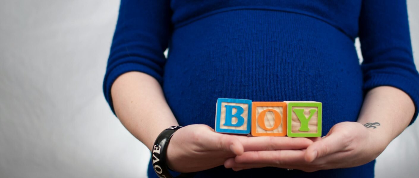 Pregnant woman in blue dress holds 'boy' blocks, symbolizing a baby boy announcement.