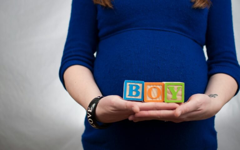 Pregnant woman in blue dress holds 'boy' blocks, symbolizing a baby boy announcement.